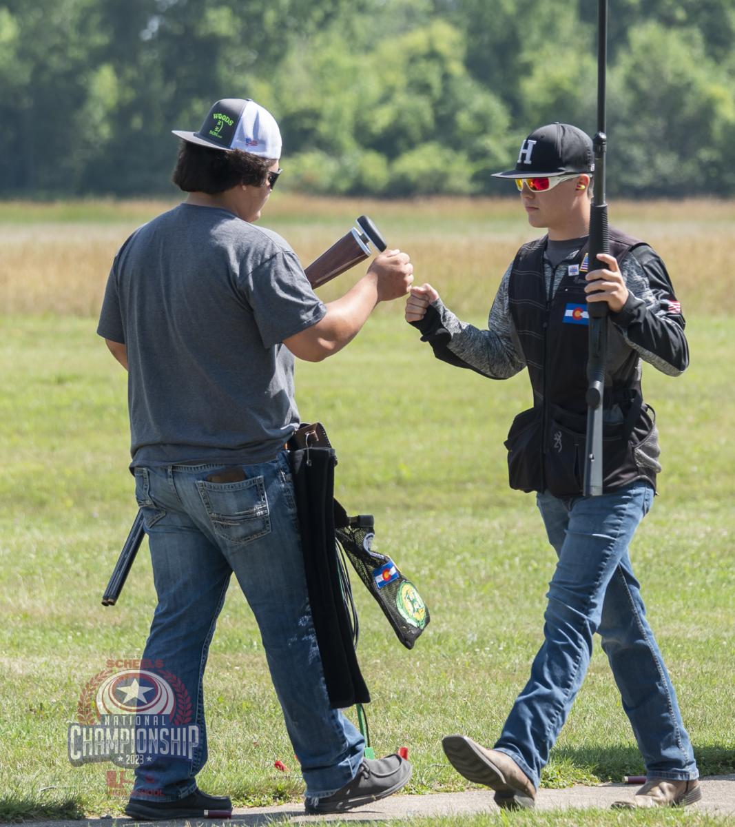 Two participants in the USA Clay Target League national championships bump their fists together as they walk past each other.